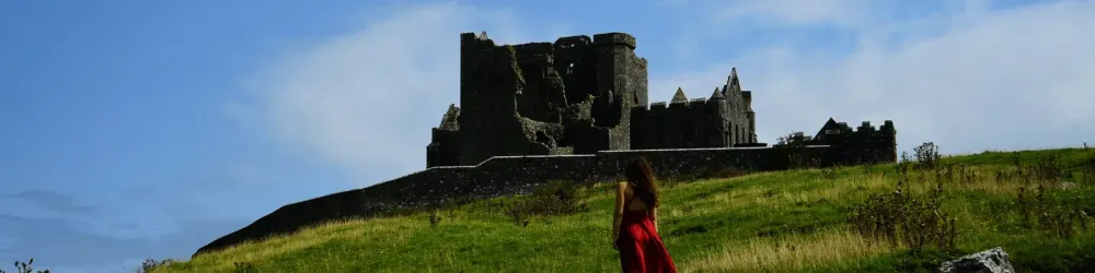Woman with wavy hairs in red dress posing in front of Medieval Rock of Casthel, Tipperary, Ireland
